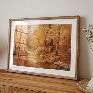 May include: A framed painting of a forest path in autumn. The trees are a mix of yellow, orange, and brown, and the path is lined with fallen leaves. The painting is in a wooden frame.
