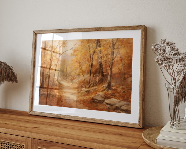May include: A framed painting of a forest path in autumn. The trees are a mix of yellow, orange, and brown, and the path is lined with fallen leaves. The painting is in a wooden frame.