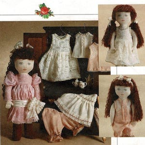 May include: Three handmade dolls with brown hair and painted faces wearing different outfits. The dolls are dressed in pink, white and peach coloured dresses. The dolls are standing in front of a wooden cabinet with a floral design on the top.