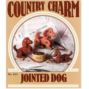 May include: A vintage sewing pattern for a jointed dog, titled "Country Charm" and "Jointed Dog" with the number 833. The pattern features three brown and white dogs with black eyes and noses, a dog bowl, and a leash.