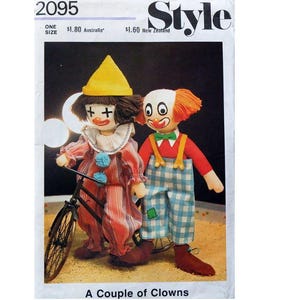 May include: A vintage sewing pattern for making two clown dolls. The pattern is titled "A Couple of Clowns" and shows a clown doll riding a bicycle and another clown doll standing next to it. The dolls are dressed in colorful clown costumes.