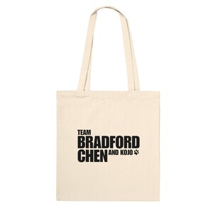Pode incluir: Uma bolsa tote de lona de cor natural com texto preto que diz "TEAM BRADFORD CHEN AND KOJO" com um símbolo de pata.