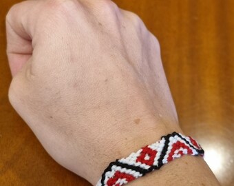 May include: A red, white, and black friendship bracelet with a geometric pattern.