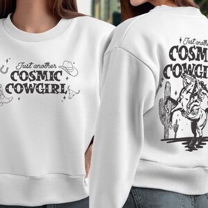 May include: White sweatshirt with a graphic print of a cowgirl riding a horse with the text "Just another COSMIC COWGIRL" on the back and the same text on the front with a cowboy boot, horseshoe, and cowboy hat.