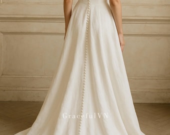 May include: A white wedding dress with a flowing skirt and spaghetti straps. The back of the dress features a row of small buttons running down the center. The dress has a simple, elegant design.