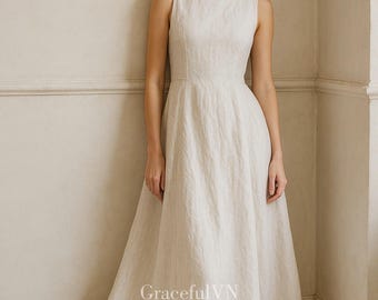 May include: A sleeveless, floor-length ivory dress with a boat neckline. The dress has a fitted bodice and a flowing skirt. The text "GracefulVN" is visible on the lower part of the dress. The dress is made of a textured fabric.