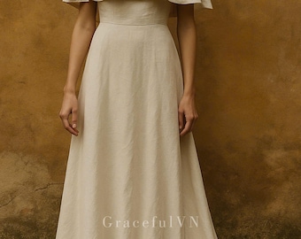 May include: A floor-length, cream-colored dress with a cape-like overlay. The dress features a fitted bodice and a flowing skirt. The text "GracefulVN" is visible near the bottom of the dress. The dress is made of a soft, flowing fabric.