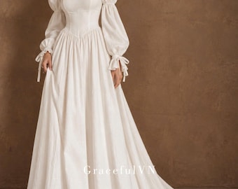May include: A floor-length white dress featuring a fitted bodice, a sweetheart neckline with ruffled trim, and long puff sleeves with tie-cuff details. The skirt is full and flowing with a train. The text GracefulVN is printed on the lower skirt.