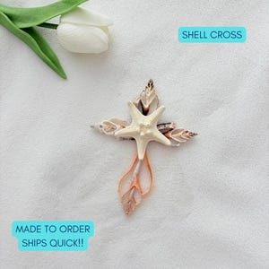May include: A cross-shaped decorative ornament constructed from various natural seashells and a central cream-colored starfish. The item is positioned near a single white tulip flower. The text SHELL CROSS is visible in a blue box, along with MADE TO ORDER SHIPS QUICK!!