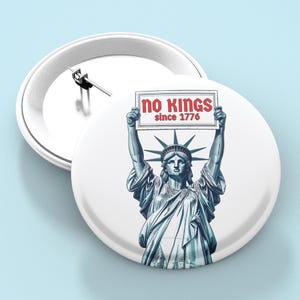 May include: White button pin featuring the Statue of Liberty holding a sign that reads "no kings since 1776" in red text. The pin has a metal clasp on the back and the words "BUTTON PIN" are in a blue box.