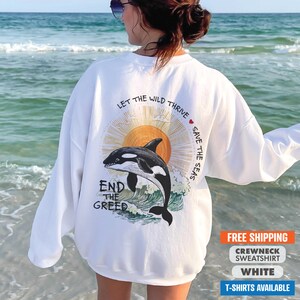 May include: White crewneck sweatshirt with a graphic of an orca jumping out of the water with a sun and the text "Let the wild thrive save the seas end the greed".