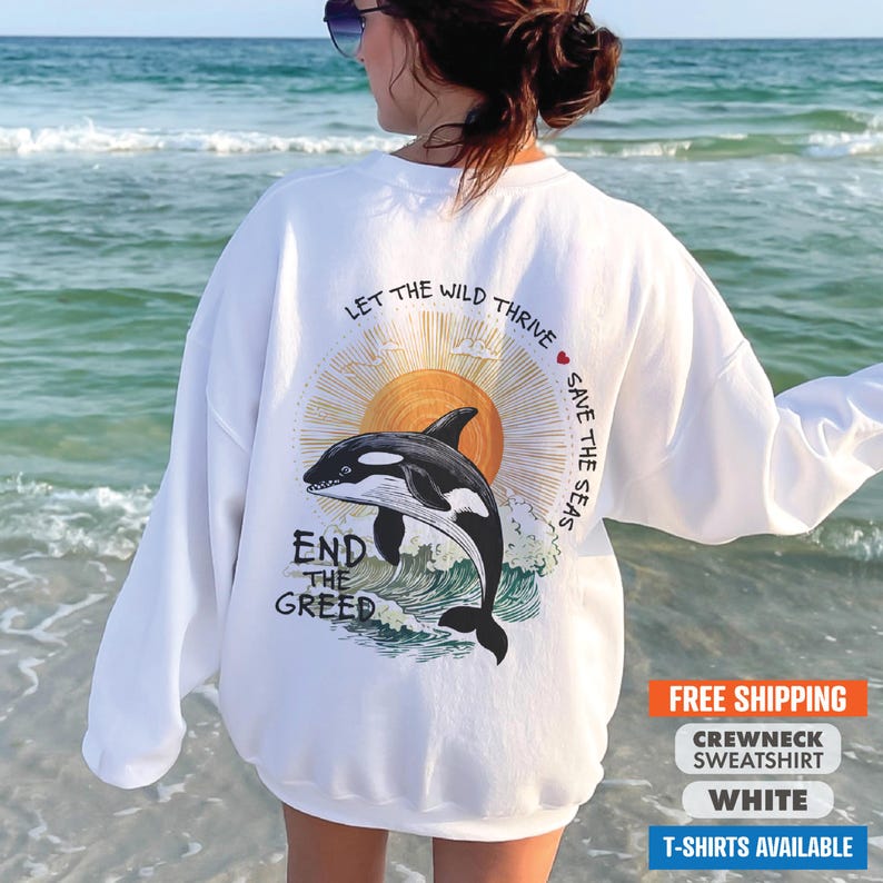 May include: White crewneck sweatshirt with a graphic of an orca jumping out of the water with a sun and the text "Let the wild thrive save the seas end the greed".