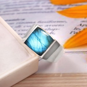 May include: A silver ring featuring a square blue labradorite gemstone. The ring has a simple, contemporary design.