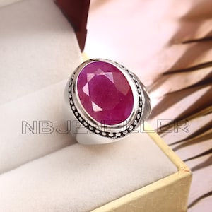 Op de afbeelding: Een zilveren ring met een grote ovale robijn. De ring heeft een parelmoerontwerp rond de rand van de zetting.