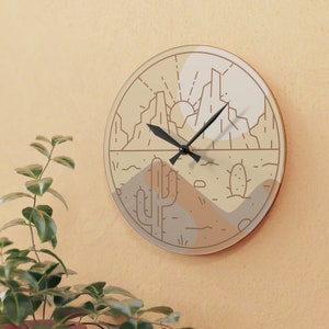 May include: A round wall clock with a beige background and a black outline. The clock face features a minimalist design of a desert landscape with mountains, a cactus, and a sun. The clock hands are black.