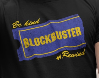 May include: Black t-shirt featuring a distressed blue and yellow graphic of a Blockbuster ticket. The text on the shirt reads "Be kind Blockbuster Rewind". The design has a vintage, retro aesthetic.