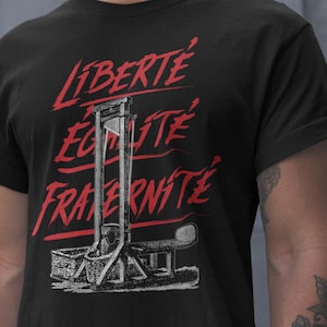 May include: Black t-shirt featuring a red and white graphic of a guillotine. The words "LIBERTE, EGALITE, FRATERNITE" are written in red above the guillotine illustration.
