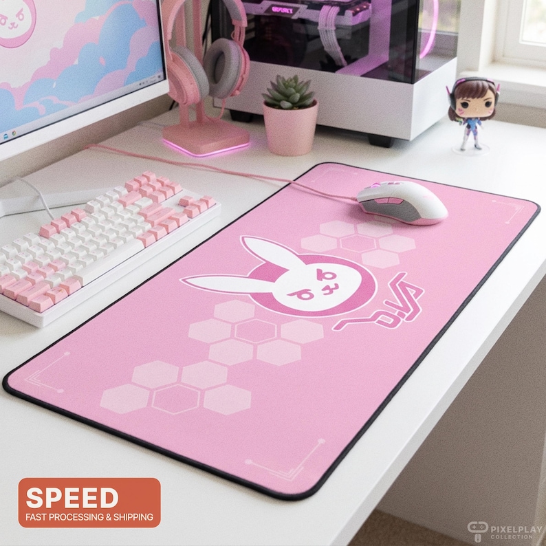 May include: Pink gaming mousepad with a white bunny logo and the word "D.Va" in a stylized font. The mousepad has a black border and a honeycomb pattern. A white and pink keyboard and mouse are also visible.