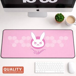 May include: A pink rectangular mousepad featuring a white bunny logo with the text "D.Va". The design includes a honeycomb pattern and a black border. The word "QUALITY" is printed at the bottom.