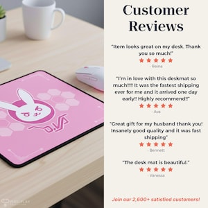 May include: Pink desk mat featuring a white bunny graphic and the text "D.Va" in a stylized font. The mat is on a light-colored wooden desk, with a white mouse and mug visible.