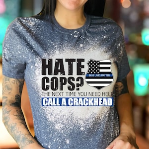 May include: A blue t-shirt with a white bleach-like design. The shirt features the text "HATE COPS? THE NEXT TIME YOU NEED HELP CALL A CRACKHEAD" and a police badge graphic with "BLUE LIVES MATTER".