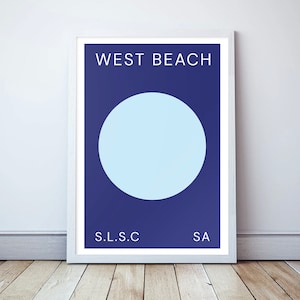 May include: A framed print with a blue background and a large light blue circle in the centre. The text "WEST BEACH" is at the top of the print, and the text "S.L.S.C" and "SA" are at the bottom.