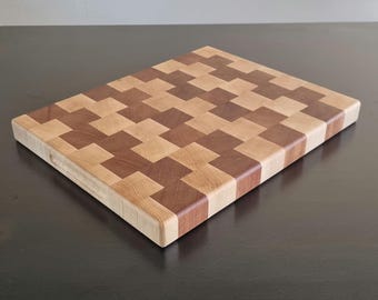 May include: A rectangular wooden cutting board with a checkered pattern of light and dark wood. The board has a handle on the side.
