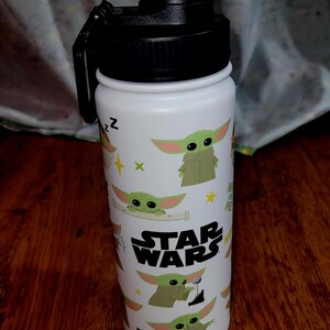 Pu&ograve; includere: Borraccia bianca con coperchio e manico neri. La borraccia &egrave; decorata con immagini di Grogu di Star Wars, insieme al logo di Star Wars. Il design include elementi verdi, gialli e bianchi.