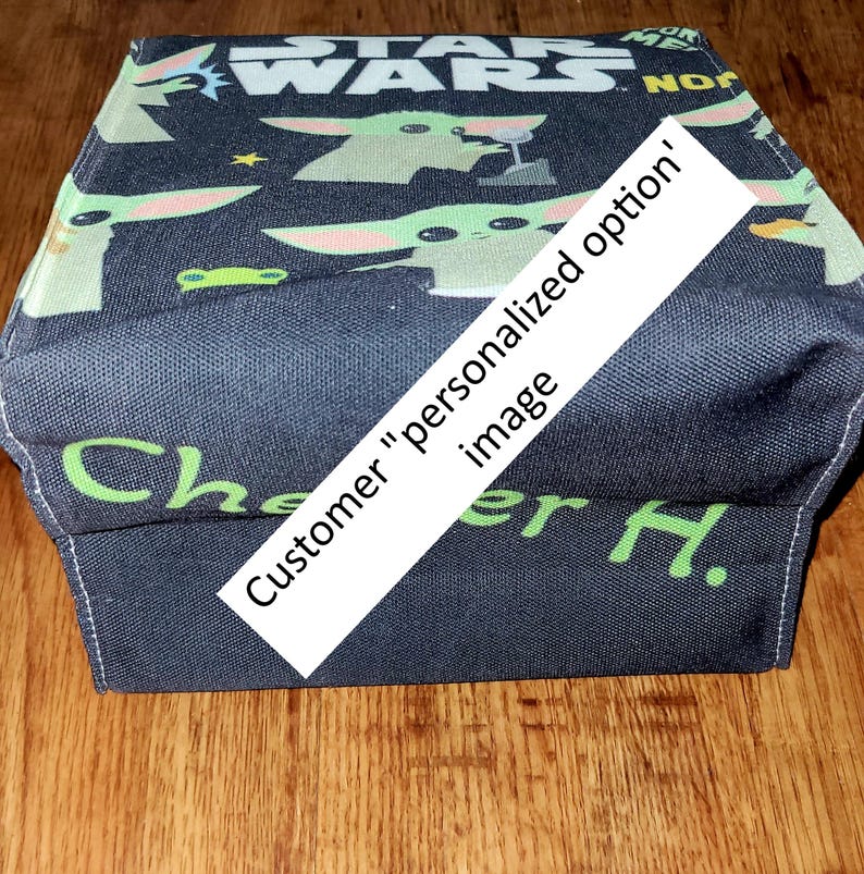 Pu&ograve; includere: Una mascherina blu scuro a tema Star Wars con Grogu e il logo di Star Wars in bianco. La mascherina ha un testo verde che dice "Che" e "er H.". Un banner diagonale bianco dice "Customer 'personalized option' image".