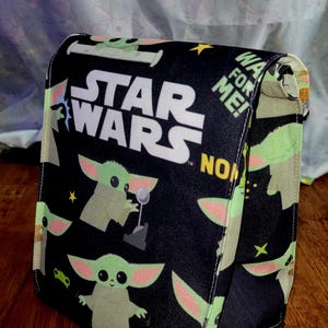 Pu&ograve; includere: Borsa nera a tema Star Wars con Grogu e il logo di Star Wars. La borsa ha una chiusura a patta ed &egrave; decorata con immagini di Grogu, stelle e le parole "WA FOR ME!" e "NOW".