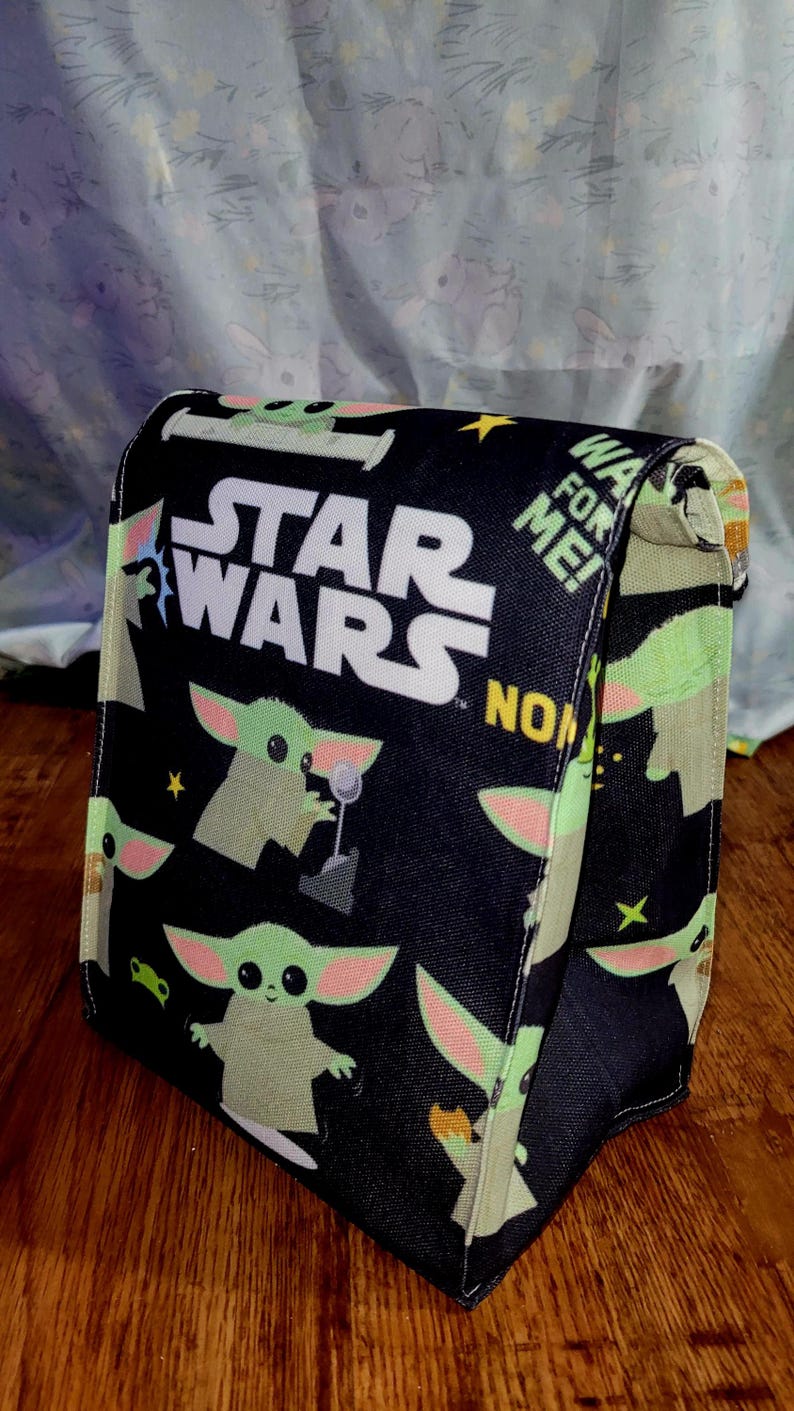 Pu&ograve; includere: Borsa nera a tema Star Wars con Grogu e il logo di Star Wars. La borsa ha una chiusura a patta ed &egrave; decorata con immagini di Grogu, stelle e le parole "WA FOR ME!" e "NOW".