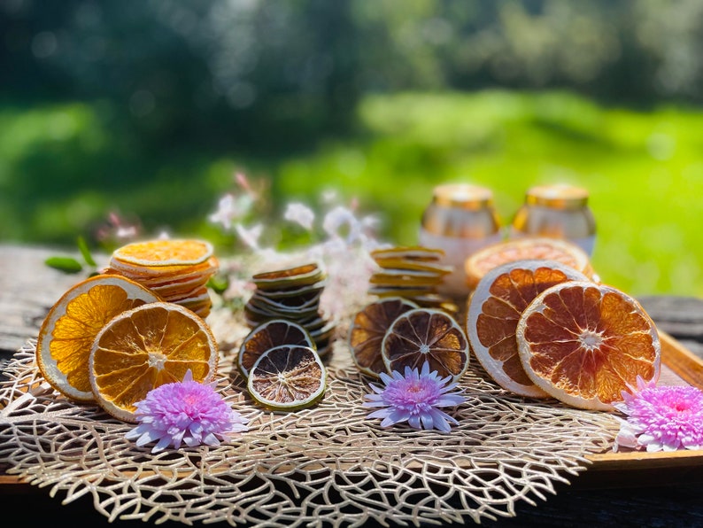 May include: Dried citrus fruit slices arranged on a woven placemat. The slices include orange, grapefruit, and lime. There are pink flowers on the placemat.