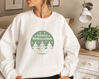 Può includere: Felpa bianca con un design circolare verde con tre alberi di Natale stilizzati e il testo "schöne Weihnachten".