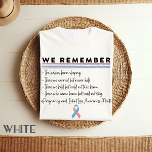 以下が含まれることがあります： 「WE REMEMBER」というテキストと、眠って生まれた赤ちゃん、抱いたことはあるけど抱きしめなかった赤ちゃん、抱いたけど家に連れて帰れなかった赤ちゃん、家に帰ったけど一緒にいられなかった赤ちゃんについてのフレーズが書かれた白いTシャツ。テキストの後に「#Pregnancy and Infant Loss Awareness Month」というハッシュタグが付けられています。テキストの下には青とピンクのリボンが表示されています。