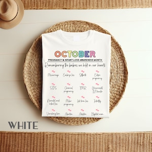 以下が含まれることがあります： 虹色の文字で「OCTOBER」と黒色の文字で「PREGNANCY & INFANT LOSS AWARENESS MONTH」と書かれた白いTシャツ。テキストの下には、流産、死産、子宮外妊娠、SIDS、化学妊娠、TFMR、IVF移植の失敗、新生児および乳児の死亡、モラー妊娠、後期流産、不妊、消失双生児、中絶、養子縁組、および空胞などの妊娠および乳児の損失の原因がリストされています。