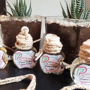 Op de afbeelding: Vier glazen flessen met gouden touw en houten doppen, gevuld met heldere vloeistof. Elke fles heeft een etiket met de tekst "L'amour Parfum" en een andere geur: "Fresh Bamboo", "Ocean Breeze", "Love" en "Fougere Marina".