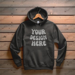 Könnte beinhalten: Ein schwarzer Kapuzenpullover mit einem großen weißen Aufdruck, der "YOUR DESIGN HERE" auf einem Holzgrund zeigt.