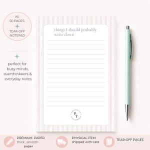 Può includere: Un blocco note rettangolare A5 a strappo con strisce verticali rosa chiaro e una sezione centrale bianca con linee orizzontali. Il testo "things I should probably write down" è stampato in alto, con un piccolo logo circolare in basso. Una penna verde chiaro è posizionata a destra del blocco.