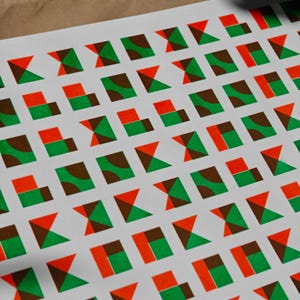 Close-up of the riso print showing rows of small geometric tiles in fluorescent orange, green and brown on white paper