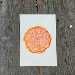 Top view of the A5 riso print on grey wooden planks, concentric tree rings in pink and yellow