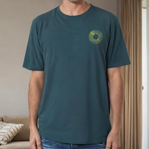 Op de afbeelding: Een tealblauw t-shirt met een geel en groen cirkelvormig ontwerp op de linkerborst.