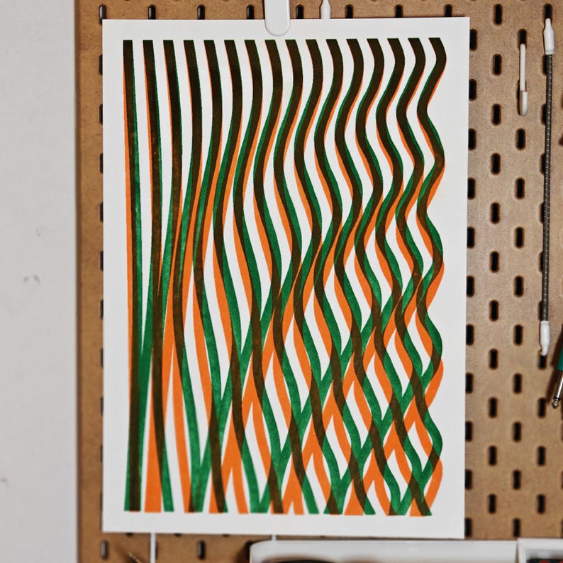 A3 risograph art print with green and orange wavy lines hanging on a wooden pegboard wall as modern abstract decor