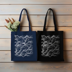 Może przedstawiać: Dwie torby typu tote z białymi abstrakcyjnymi wzorami linii na drewnianym tle. Torba po lewej stronie jest granatowa, a torba po prawej stronie jest czarna.