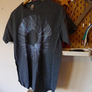 Dark heather grey t-shirt hanging on a pegboard showing the abstract blue radial circle print, studio setting
