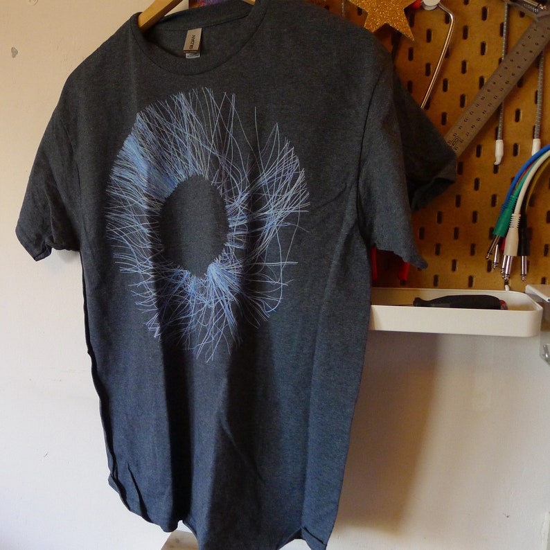 Dark heather grey t-shirt hanging on a pegboard showing the abstract blue radial circle print, studio setting