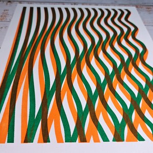 Angled view of the handmade riso print showing wavy green, orange and brown lines flowing across thick white paper