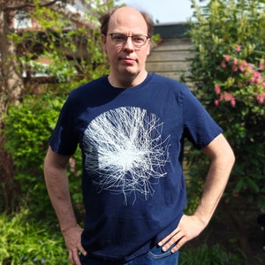 Man in a garden wearing the navy t-shirt with the white generative particle print, hands on hips