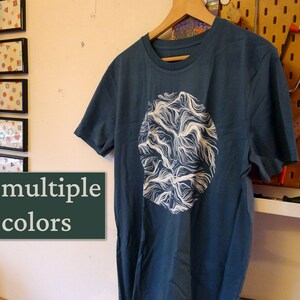 Könnte beinhalten: Ein blaues T-Shirt mit einem weißen, kreisförmigen Grafikdesign aus wirbelnden Linien.