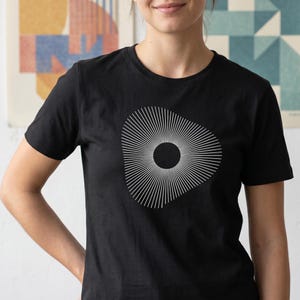 Op de afbeelding: Zwart T-shirt met een wit geometrisch ontwerp. Het ontwerp is een cirkel met uitstralende lijnen, waardoor een sunburst-effect ontstaat. Het shirt is gemaakt van een zacht materiaal en is geschikt voor vrijetijdskleding.