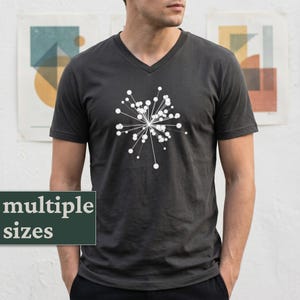 Może przedstawiać: Ciemnoszara koszulka z dekoltem w serek z białym wzorem rozbłysku gwiazdy. Koszulka ma krótkie rękawy i dekolt w serek. Tekst "multiple sizes" jest wyświetlany na zielonym prostokącie.